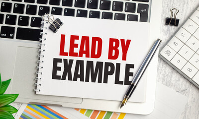 lead by example text on notepad and laptop on wooden background
