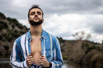 Portrait of a stylish young man opening his shirt with his head tilted back in nature.