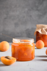 Apricot jam in glass jar for winter on gray background. Summer harvest and canned food. Tasty...