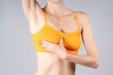 Breast test, woman in yellow bra examining her breasts for cancer on gray background