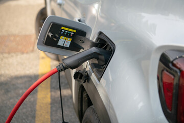 electric car being recharged, connected with the red cable to the electrical control unit, where it draws energy, in a dedicated parking lot. Zero emissions in cities with green ecological policies.