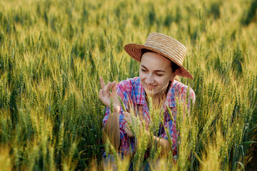 A young farmer in a checkered shirt sits in the ears of wheat and rejoices in the harvest