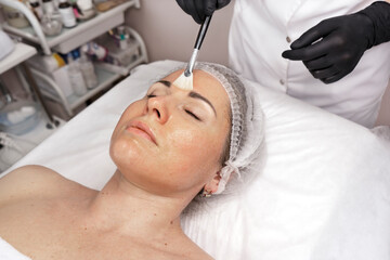 Moisturizing rejuvenation facial peeling mask. Medicine and cosmetology. Beautician's hands in black gloves do facial massage and peeling at the spa salon. Skin and body care, spa beauty treatment.