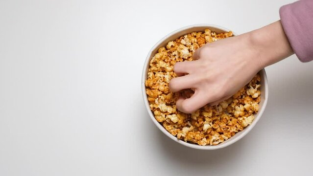 Top view on Hand greedily takes popcorn from a paper bucket isolated on white background. Hands grab popcorn. Bowl of sweet caramel popcorn