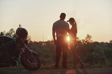 Obraz na płótnie Canvas Young beautiful couple motorcyclist hugging at sunset, traveling together on a motorcycle