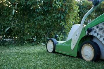 Electric lawn mower on freshly mowed grass with green hedge in the background