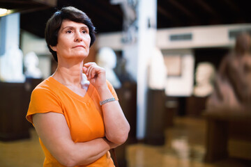 Thoughtful middle aged glad smiling lady examining exposition in museum hall of ancient sculpture.