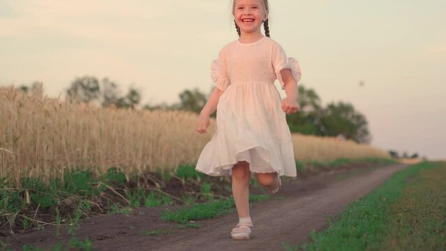 Little happy girl runs road in wheat field, slow motion. Childhood dream concept. Girl smiling playing at sunset, Kid runs outdoors. Happy family concept, childhood dream, child in field at sunset