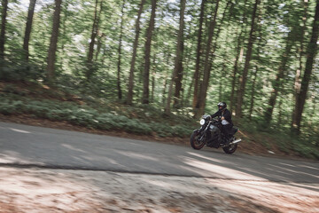 A young man biker in a helmet quickly rides at high speed on a forest road, in motion