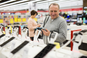 Attentive European man chooses a mobile phone in an electronics store to buy it