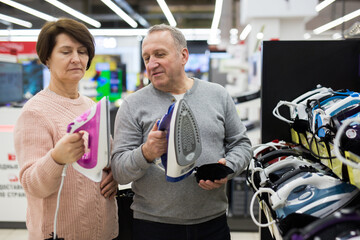 Fototapeta na wymiar Happy spouses of mature age, who came to the electronics and home appliances store, choose an iron to buy it