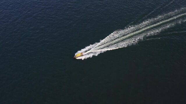 A yellow speedboat sails at high speed on the surface of the sea. An aerial drone shot over a speedboat with small waves in the ocean. Fast scooter in the sea from above.