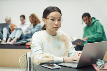 Fototapeta premium Serious teenage girl concentrating on schoolwork while sitting in front of laptop and looking for online information for new project