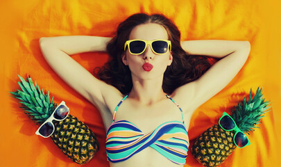 Portrait of young woman lying on the beach with funny pineapple wearing sunglasses