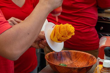 Mexican mango flower or mango on a stick being made by a street vendor at a market. The fruit is orange color and the vendor is sprinkling lime, chili, salt and cinnamon over the sticky sweet fruit. 