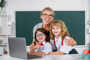 Back to school. Kids learning with teacher. Children from elementary school study at lesson. Boy and girl with teacher learn english language or mathematics on laptop.