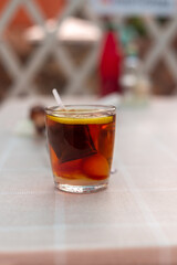A glass of hot black tea with a slice of lemon on a light tablecloth