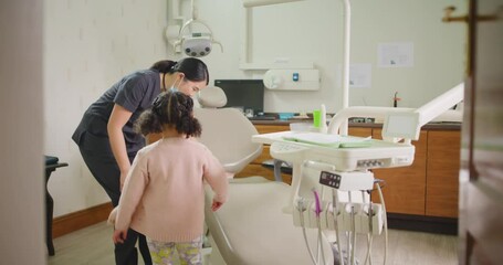 Dentist calling little girl to examine her teeth during fun dental appointment. Cheerful kid giving high five and ready for her routine checkup. Child learning about oral and dental hygiene