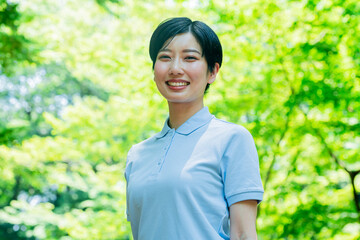 新緑の中、笑顔で笑うポロシャツを着た日本人女性