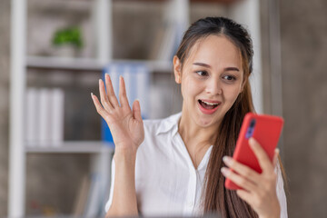 Happy Asian young woman waving hands looking at web camera using phone for video call at home,...