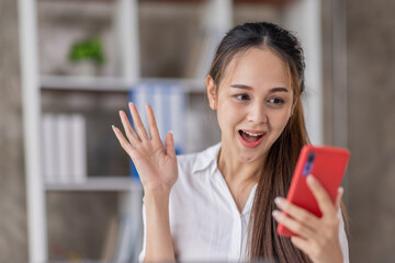 Happy Asian young woman waving hands looking at web camera using phone for video call at home,...