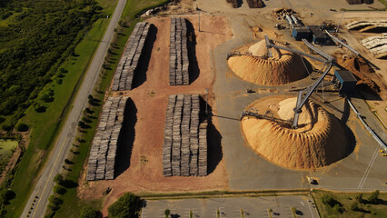 Piles of trunks and sawdust mountains in paper mill factory. Fray Bentos in Uruguay. Aerial top-down directly above