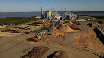 Aerial view of Paper Mill Factory with smoky chimneys front to River - Sawdust piles and pipes...