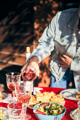 A woman pours wine into glasses. A full table is set for a friendly banquet outside. Vertical photo.