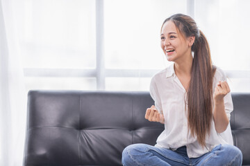 Excited young Asian woman on sofa in home office