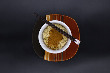 Dried noodle in a white plastic bowl on an orange and brown plate.