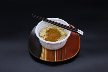 Dried noodle in a white plastic bowl on an orange and brown plate.