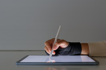 Female hand using pen to draw design on tablet screen with wrist protector attached.