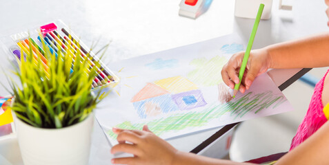 Asian cute kid preschooler sit on table smile she draw country house picture with pencil at home to...