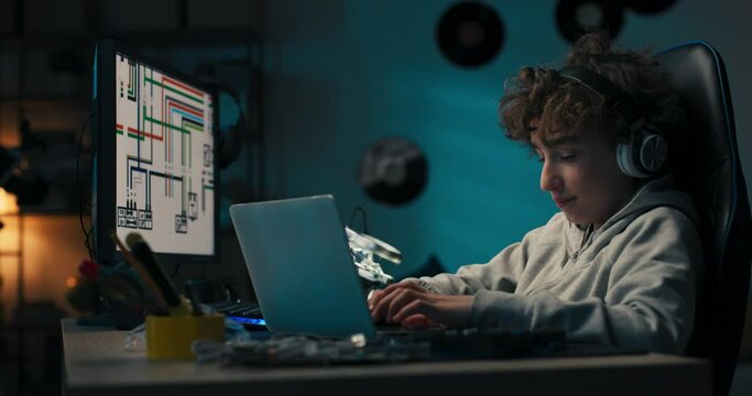 A Young Boy Sits At His Desk With Wireless Headphones In Front Of A Computer Taking Notes With A Pencil, Drawing A Design, Passionate About Architecture.