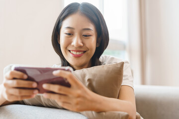 Home lifestyle concept, Young woman sit on couch and hug pillow to play games on smartphone at home