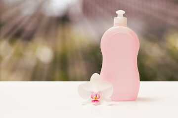 Bottle of dishwashing liquid and orchid flower on blurred background.