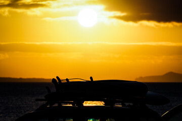 Fototapeta na wymiar Surfboards on car roof at sunset with yellow sky