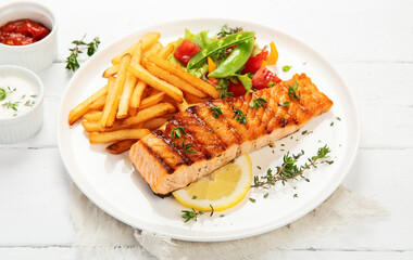 Salmon steak with vegetables and fries on light background.