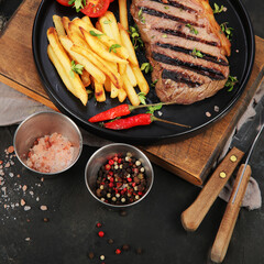 Striploin beef steak with french fries on dark background.