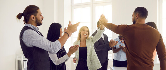 Fototapeta Happy multiracial business team celebrating success. Smiling young man and woman give each other high five while office colleagues are applauding. Successful teamwork concept. Banner header background obraz