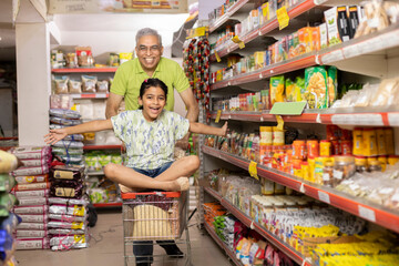 Grandfather is giving his granddaughter a ride in the shopping trolley while they're buying food in...