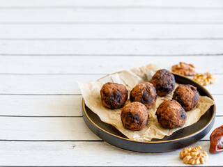 Healthy homemade delicious energy balls: chocolate ball cakes made from raisin, prune, dates, walnut, figs in black plate against white background, covered with cocoa carob powder. Close up copy space