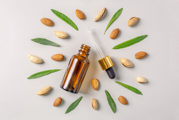 Glass bottle with a pipette and nuts and leaves of almond on a gray background