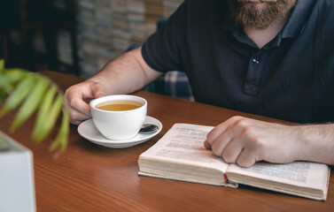 Close-up, a cup of tea and a book in male hands.