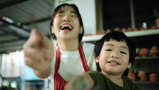 Happy and funny family moment Mother teaching son how to painting and playing to camera. Child creative activities and art. Kid playing  pottery workshop. Developing children's learning skills.