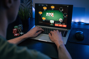 Young man play online poker in laptop. - obrazy, fototapety, plakaty