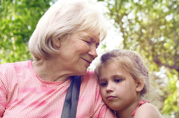 Loving cute granddaughter hugging  her grandmother and talking about little secrets. Happy family.  Having good times with grandparent outdoors.