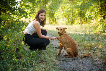 Cheerful young beautiful woman hugging her pretty dog in forest