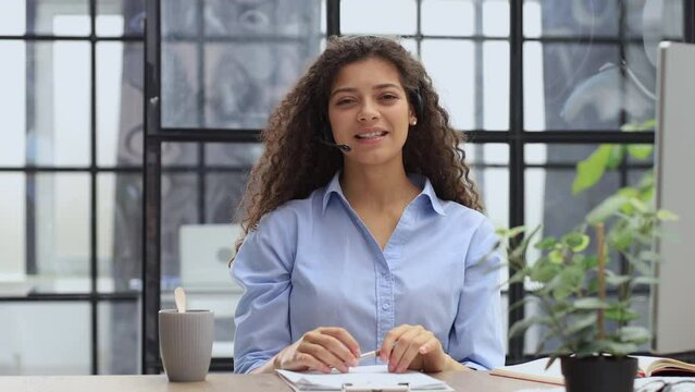 Young call operator businesswoman wears headset customer service manager looking and speaking to webcam, communicating in distance remote chat