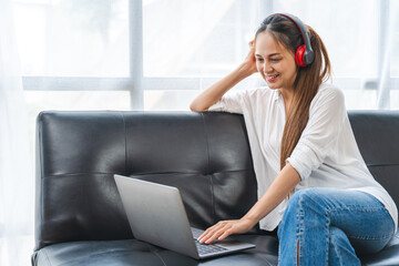 Young business freelance Asian woman working on laptop checking social media news while sitting on sofa.